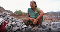 A widow in India sitting among stones at a work site