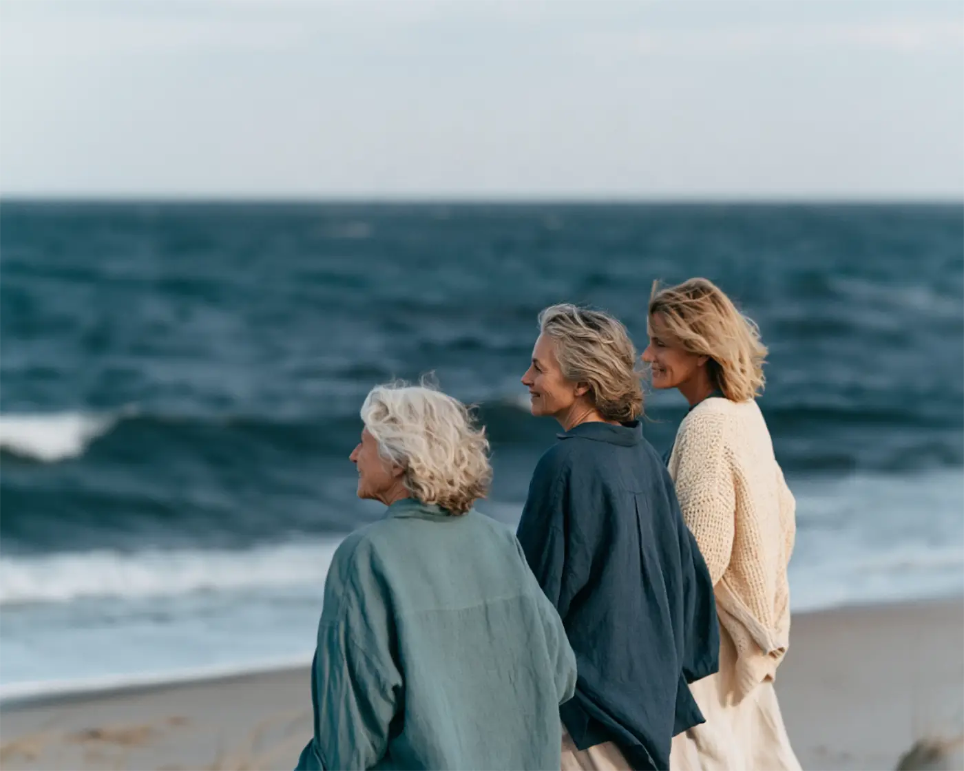 Three women chatting together on a sandy beach with the blue sea in front of them